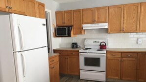 Una cocina con armarios de madera, un refrigerador blanco, un microondas, una tetera y una estufa.