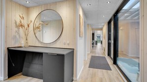 Ett modernt receptionsområde med en väggpanel i trä, en rund spegel, ett skrivbord och en glasdörr som leder ut till en balkong.