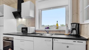 Une cuisine moderne avec des meubles blancs, un four à micro-ondes encastré, une machine à café et une fenêtre donnant sur l’extérieur.
