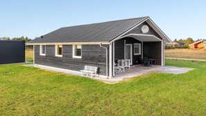 Un petit bâtiment d’un seul étage, à l’extérieur sombre, doté d’un toit en pente et d’un porche abrité avec un banc et des chaises.