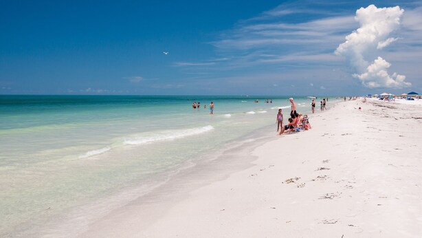 A beach with clear turquoise water, white sand, and a few people enjoying the sun.