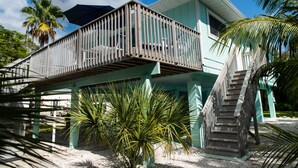 A two-story house with a balcony, palm trees, and a staircase.