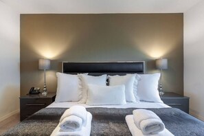 A neatly made bed with white linens, two bedside lamps, and a telephone on the nightstand.