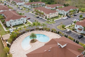 A residential area with a swimming pool surrounded by lounge chairs and palm trees.