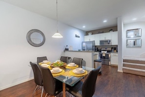 A modern kitchen with white cabinets, stainless steel appliances, and a dining area with a glass table and black chairs.