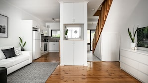 A modern kitchen with white cabinetry, a wooden staircase, and a dining area with a white table and chairs. - View One Three (Seaton)