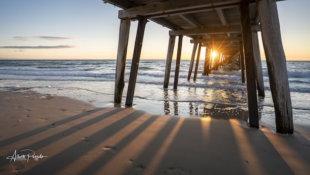 A wooden pier extending into the ocean with the sun setting in the background. - View One Three (Seaton)