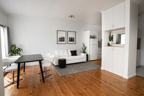 A modern living room with a white sofa, a black coffee table, and a grey rug. There is a white cabinet and a small plant on the right.