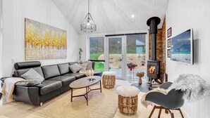 A modern living room with a black leather sofa, a round coffee table, and a fireplace. - 4 bedroom stunning home in Sjølund (Sjølund)