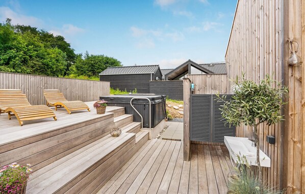 Une terrasse en bois avec des chaises longues, un jacuzzi et un petit jardin agrémenté de plantes et de fleurs.