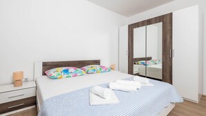 Ein Schlafzimmer mit einem Bett, zwei Kissen, einem Nachttisch, einer Lampe, einem Spiegel und einem Kleiderschrank.