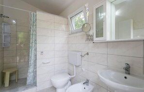 Casa de banho com sanita, bidé, lavatório e janela com vista para árvores.