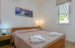 Quarto com cama, mesa de cabeceira, luminária, pintura e janela.