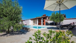 A pool area with a tiled deck, a barbecue setup, and a covered seating area with an umbrella. - Stunning home in Galizana (Galizana)