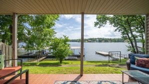 Une terrasse couverte avec vue sur un lac, des meubles d’extérieur et un tapis à motifs.