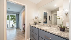 Une salle de bain moderne avec un grand miroir, un comptoir en marbre et deux orchidées en pot.