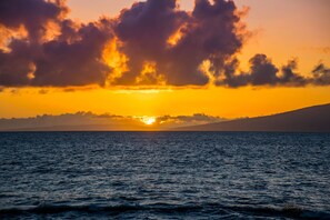 A sunset over a calm sea with a distant shoreline. - Ocean views with Hawaiian-inspired decor (Lahaina)