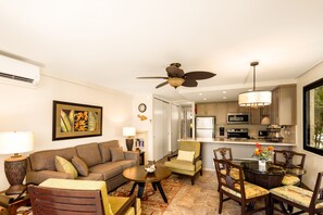 A living room with a sofa, armchairs, a coffee table, and a dining area with chairs and a table. There is a kitchen visible in the background. - Ocean views with Hawaiian-inspired decor (Lahaina)