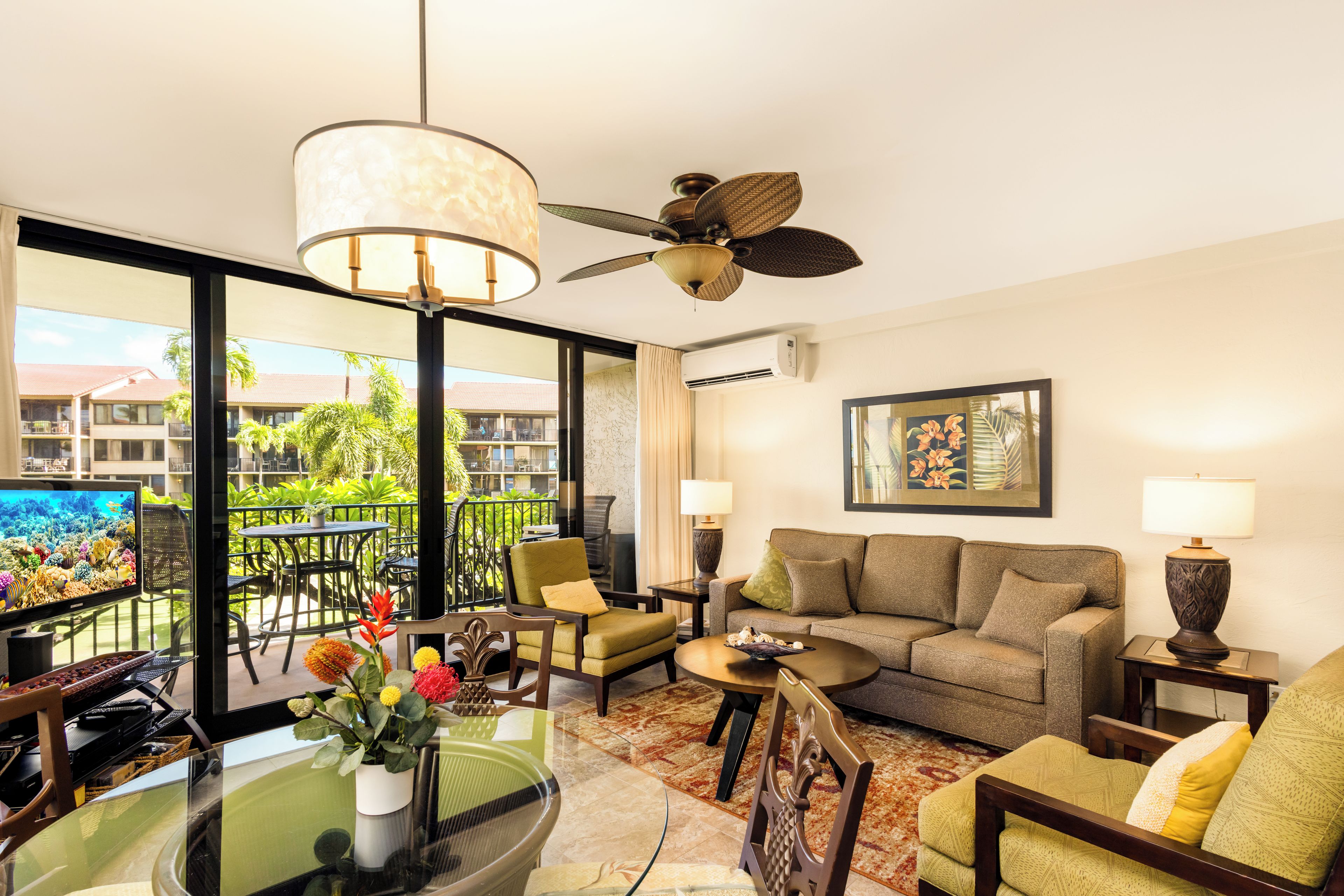 Una habitación de hotel con balcón, sofá, mesa de comedor y ventilador de techo.