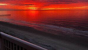 A sunset over a beach with a pier extending into the water.