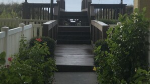 A wooden staircase leading to a deck with railings, surrounded by greenery and a cloudy sky.