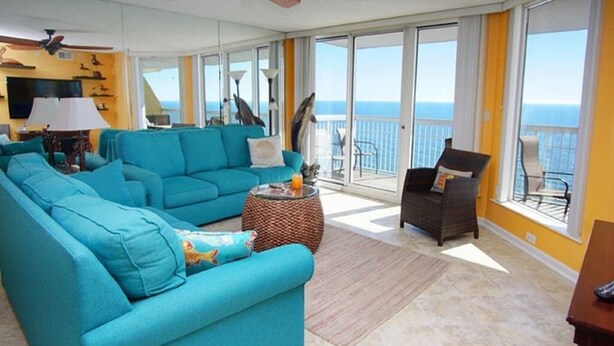 A spacious living area with a large sofa, a smaller sofa, and a chair, all facing a balcony with a view of the ocean.