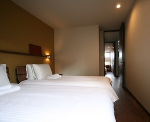 A hotel room with a large bed, a bedside table, a wall-mounted light, and a door leading to another room.