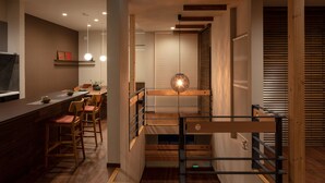 Ein modernes Interieur mit einer Holztreppe, einem Essbereich mit Stühlen und einer Küchenzeile mit Arbeitsfläche und Barhocker.