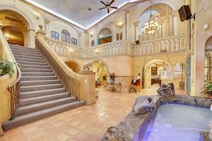 A grand interior with a central staircase, a hot tub, and a balcony with ornate railings.