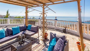 Un espace extérieur aménagé, abrité et doté d’une vue sur la mer, comprenant un ensemble de canapés et une table.