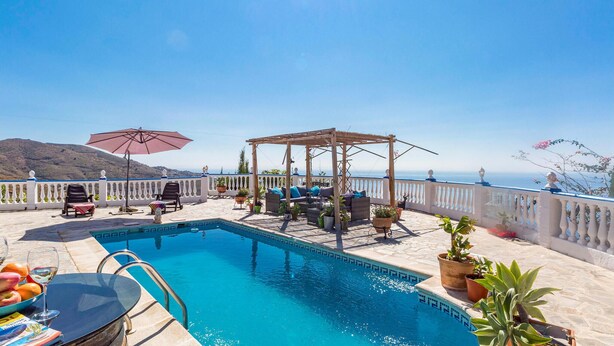 Un espace piscine aménagé sur le toit, avec une pergola, des chaises longues et une vue sur la mer.