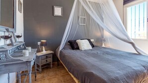 Une chambre à coucher avec un lit sous un dais, une table de chevet avec une lampe, une commode et un tableau encadré au mur.