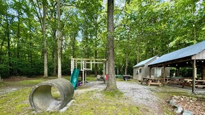 A rustic cabin with picnic tables and a play structure in a wooded area. - Country Escape Home in the Woods- Chesapeake, VA (Chesapeake)
