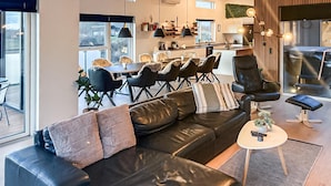A modern living room with a black leather sofa, a dining area with a round table and chairs, and a kitchen in the background. - Lovely home in Spøttrup with WiFi (Spøttrup)
