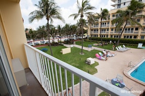 A hotel pool area with palm trees, lounge chairs, and a swimming pool. - Large Beach Front Studio in an upscale full service beach resort. (Pompano Beach)