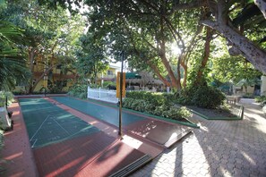 A courtyard with a shuffleboard court, surrounded by trees and a building with balconies. - Large Beach Front Studio in an upscale full service beach resort. (Pompano Beach)