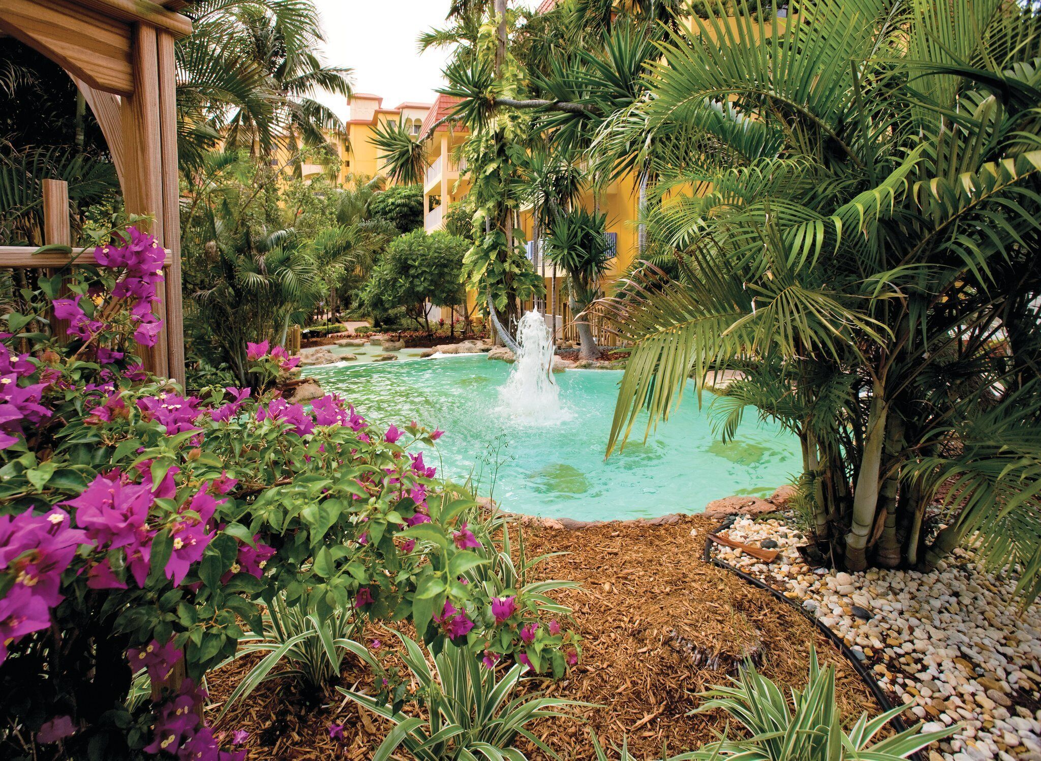 A tranquil garden with a central water feature, lush greenery, and a wooden pergola.