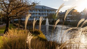 Uitzicht op een meer met op de voorgrond een gebouw, een fontein en een boom.