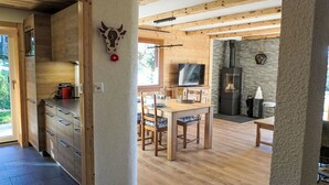 Een moderne keuken met houten kastjes, een eethoek met een houten tafel en stoelen, en een stenen open haard.