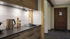 Een moderne keuken met een houten aanrecht, een roestvrijstalen waterkoker en een houten deur op de achtergrond.