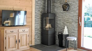 Een moderne woonkamer met een houten kast, een zwart houtkacheltje en een televisie op een houten dressoir.