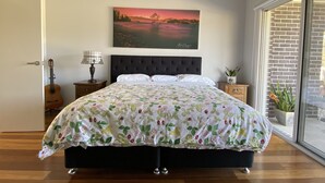 A bedroom with a bed, a guitar, a lamp, a painting, and a view of the outdoors.