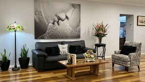 A modern living room with a wooden herringbone floor, a black leather sofa, a patterned armchair, a coffee table, and a floor lamp.