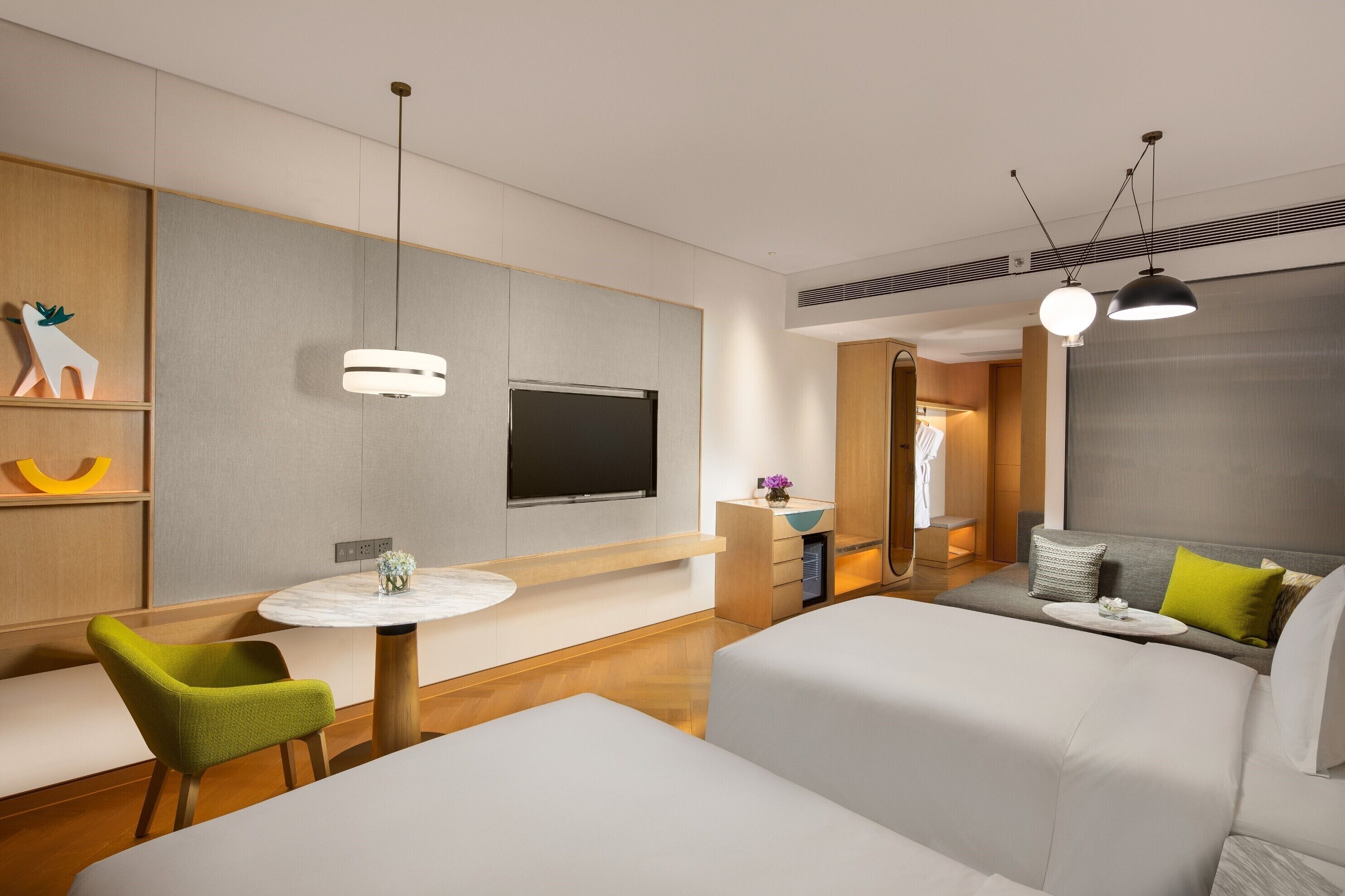 A modern hotel room with a flat-screen TV, a round dining table, a sofa, and a bed.