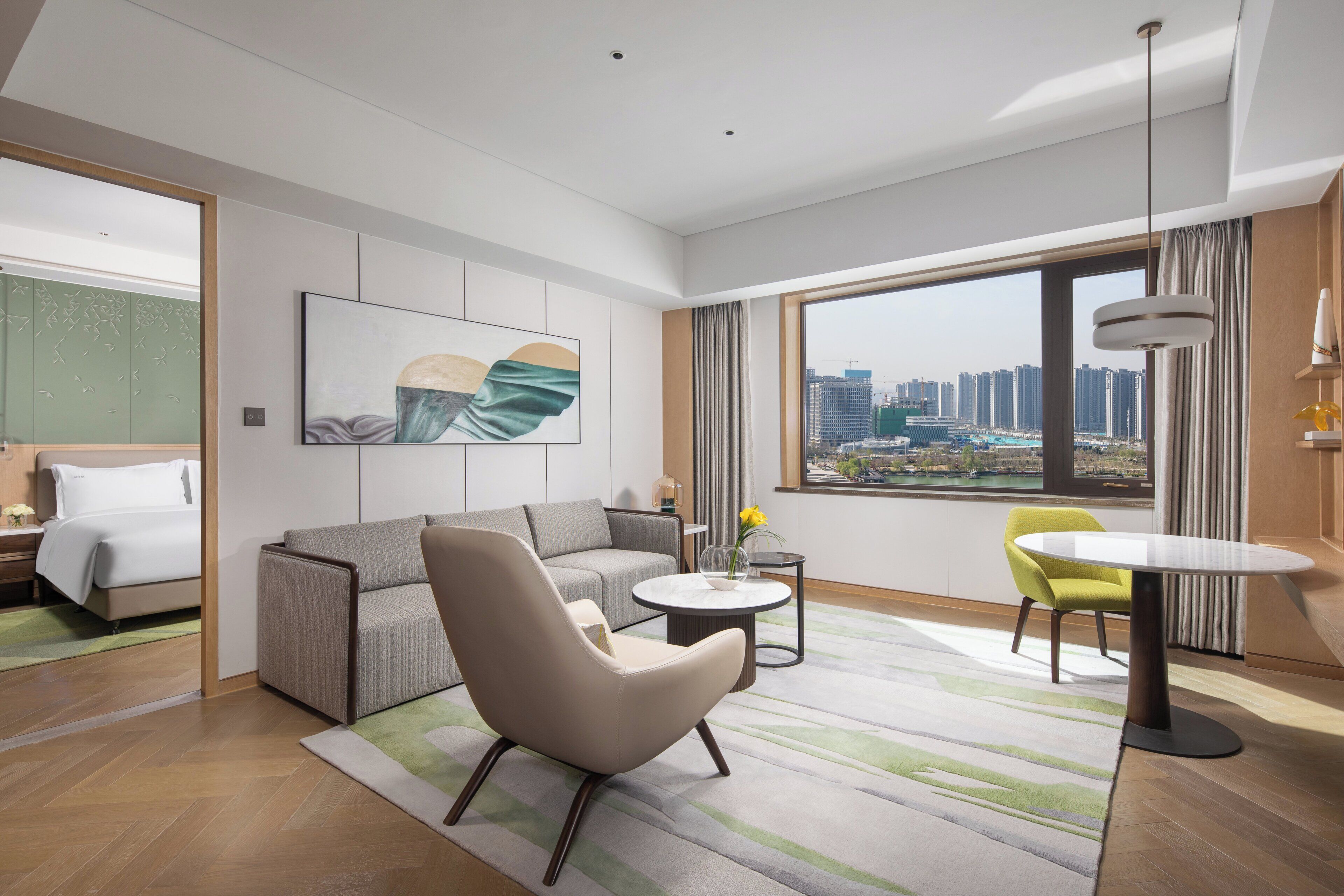 Habitación de hotel moderna con sofá, sillón, mesita y vistas a la ciudad.