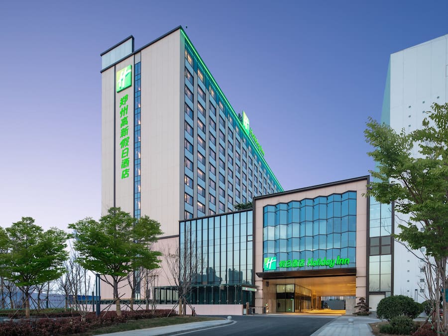 A hotel with a modern facade, large windows, and a prominent green sign.
