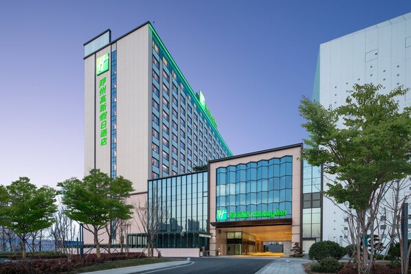 A hotel with a modern facade, large windows, and a prominent green sign. - Holiday Inn Zhengzhou High Tech Zone by IHG (Zhengzhou)