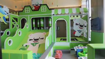 Un área de juegos infantiles con decoración verde y blanca, que incluye un tobogán con tema de oso y zonas de juego con redes.