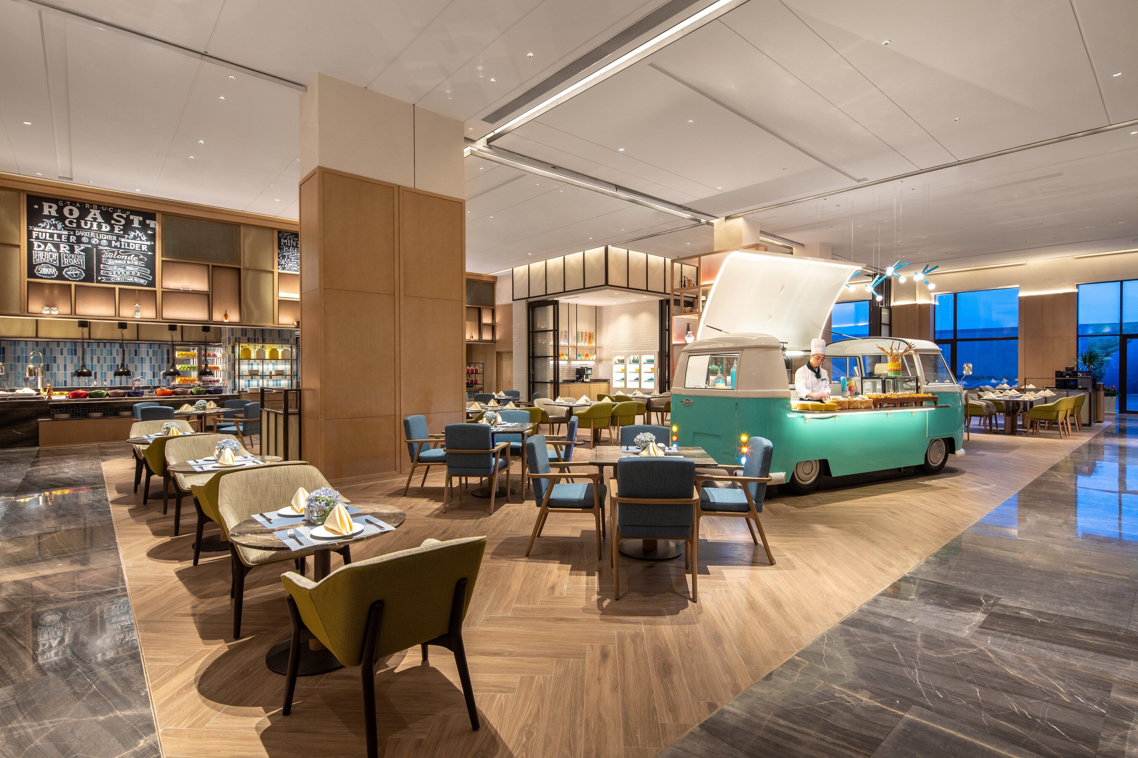 A modern restaurant with a central food truck, multiple seating areas, and a variety of food displays.