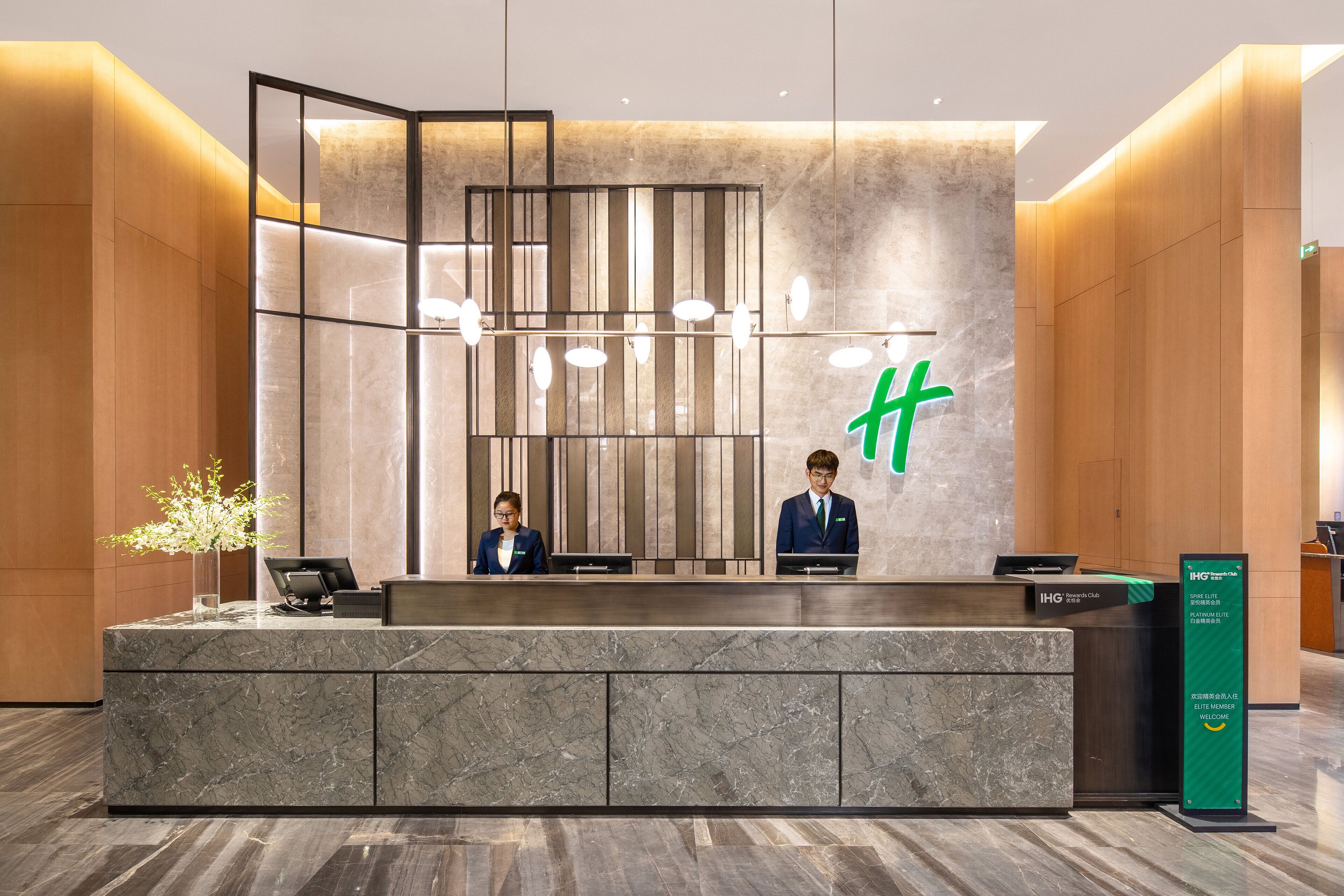 A reception desk with two staff members, a modern design with a marble counter, and a green signboard.